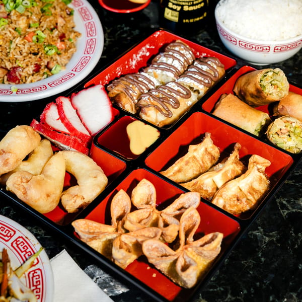 A Chinese bento box filled with various dishes, including fried wontons, dumplings, and egg rolls.