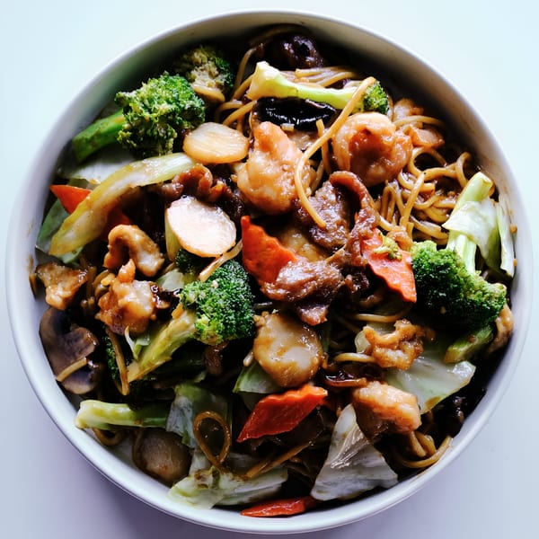 A large bowl of Chinese lo mein noodles with shrimp, beef, broccoli, and other vegetables.