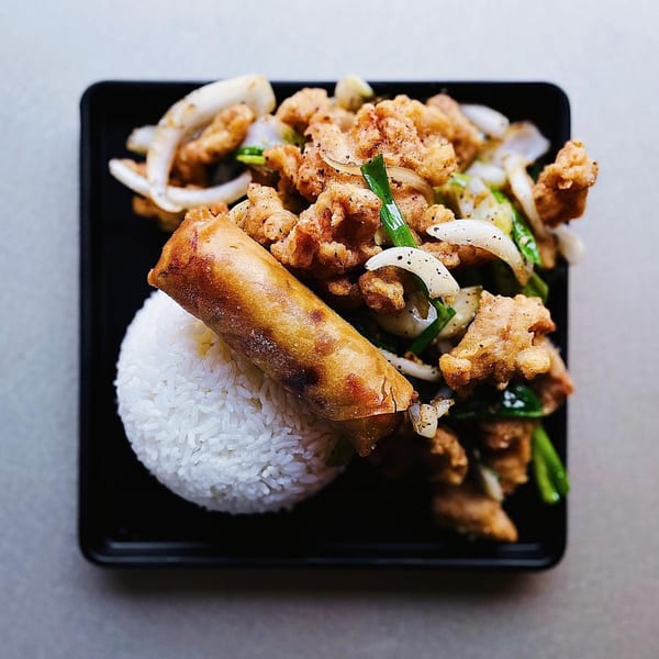 A Chinese dish with fried chicken, onions, green onions, and an egg roll, served with white rice.