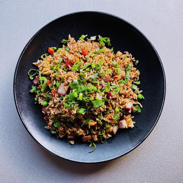 A black bowl filled with Chinese fried rice, topped with chopped green onions, red peppers, and pork.