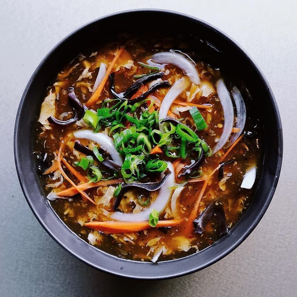 A black bowl of hot and sour soup with carrots, onions, mushrooms, and scallions.